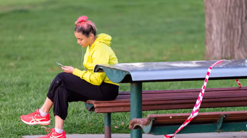 A woman sits at a park bench checking her phone